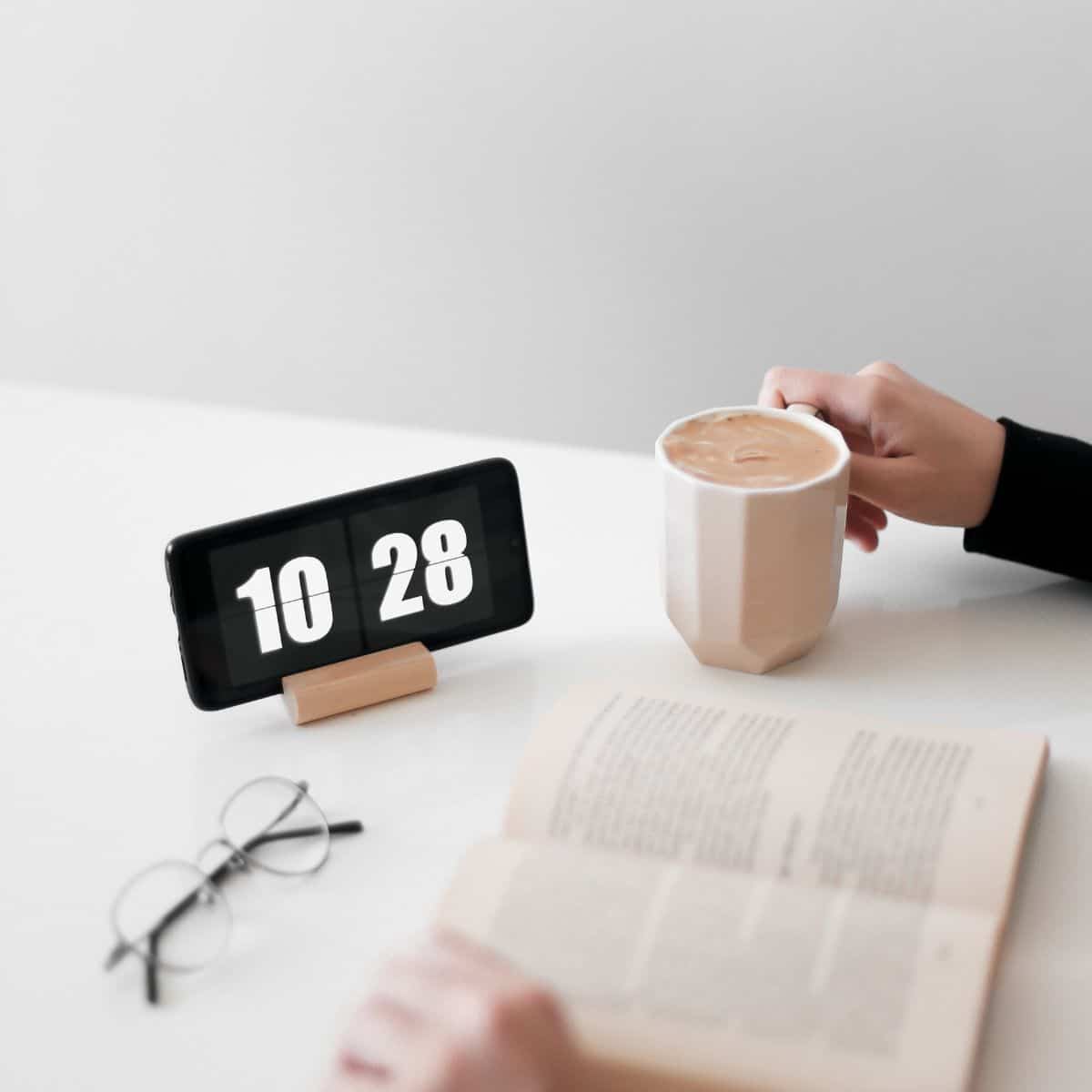 person reading a book near a clock with a cup of coffee