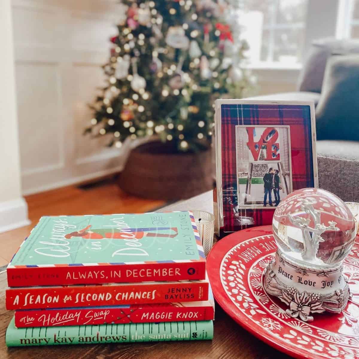 stack of Christmas romance books in front of tree and near holiday decor.