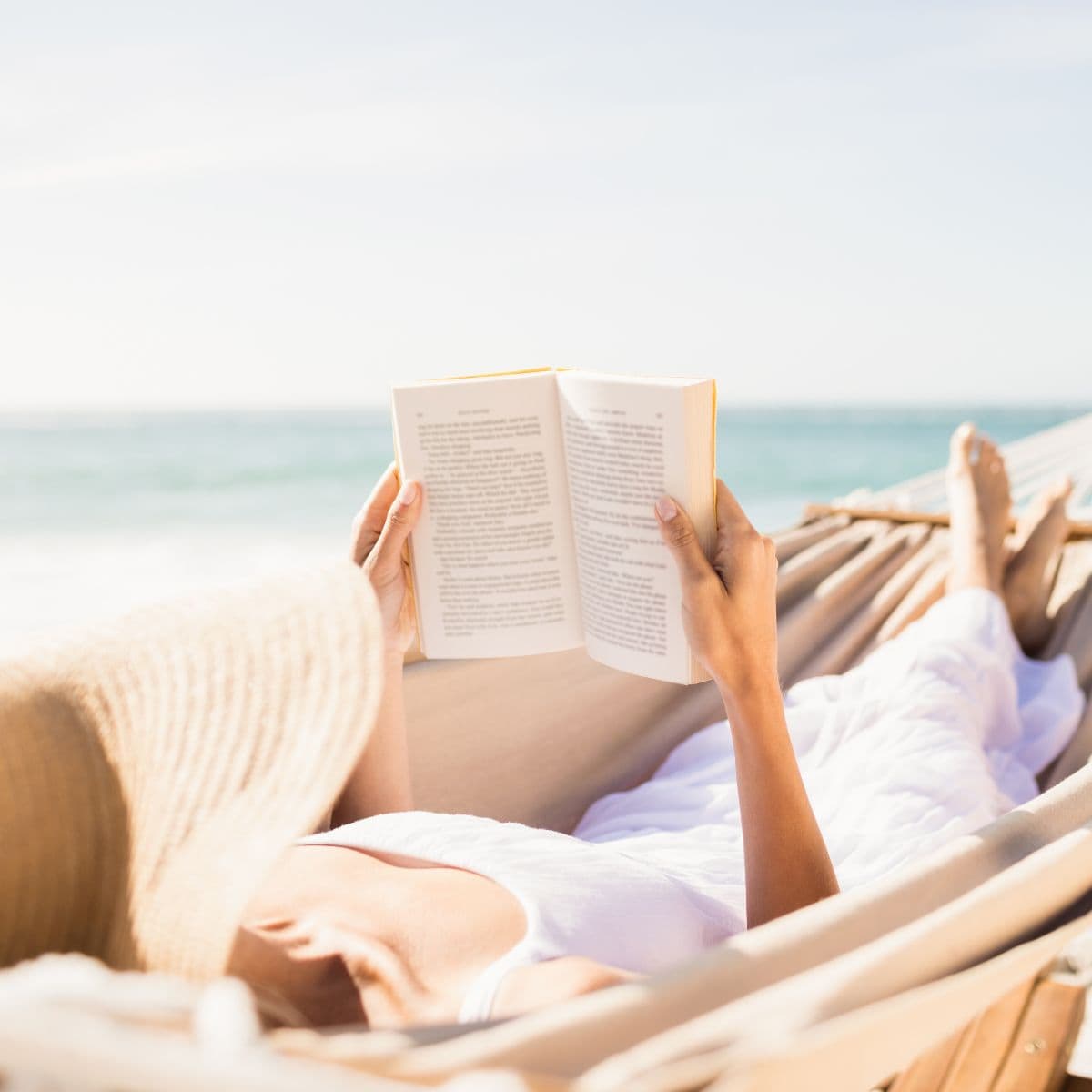 woman reading a book on the beach in a hammock.