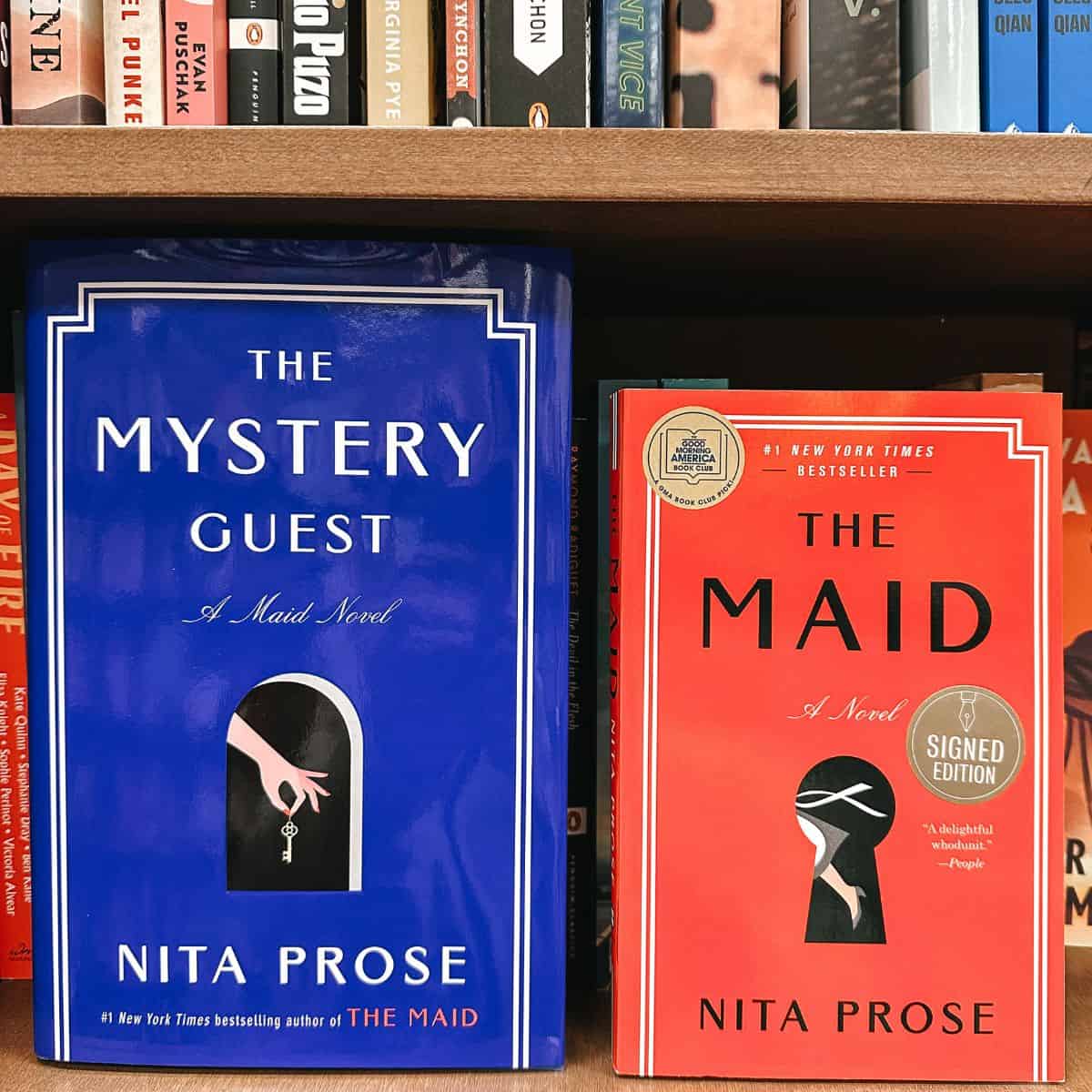 the mystery guest and the maid by nita prose in front on bookshelves.