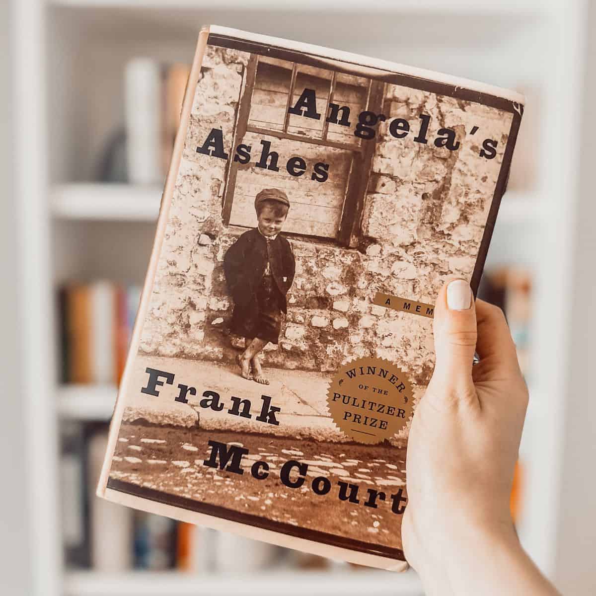 Angela's Ashes by Frank McCourt held in front of a bookshelf.