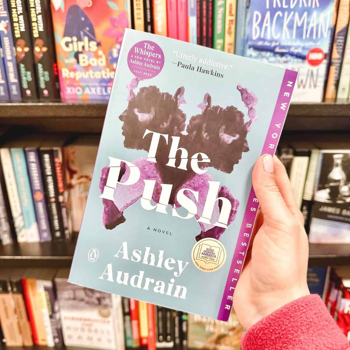 The push by Ashley audraine held in front of a bookshelf.