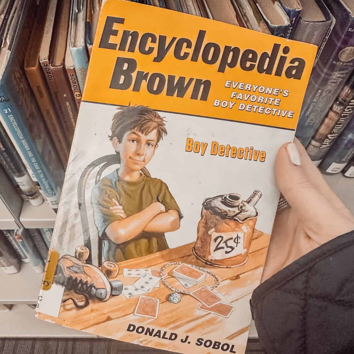 encyclopedia brown by donald j. sobol held in front of a bookshelf.