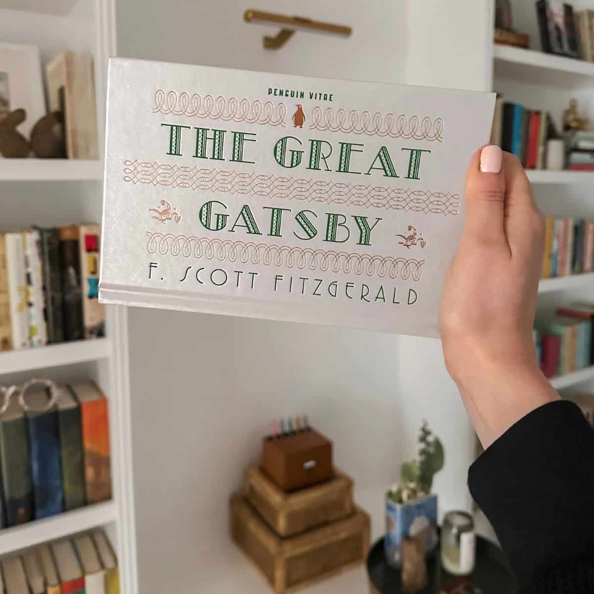 f. scott fitzgerald, the great gatsby held in front of bookshelves.